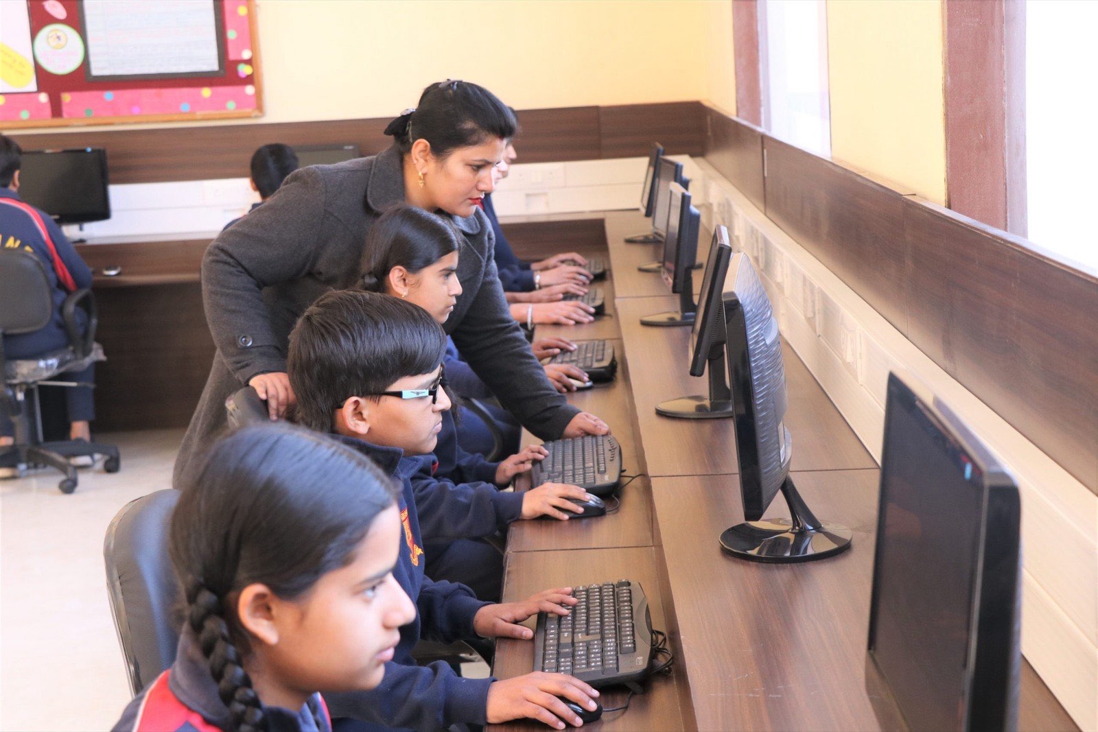 A teacher assisting students working at computers in the computer laboratory